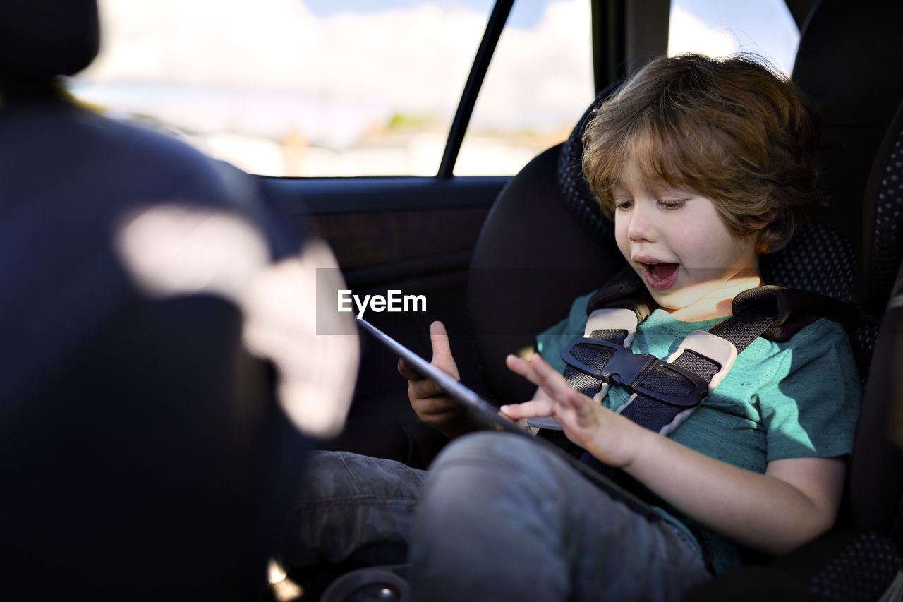 Cute boy using digital tablet while sitting in car