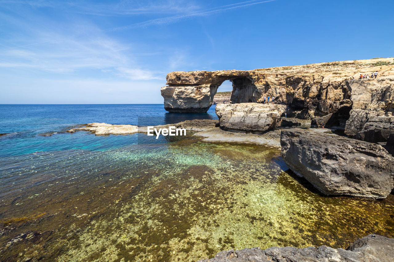 Scenic view of sea by cliff against blue sky