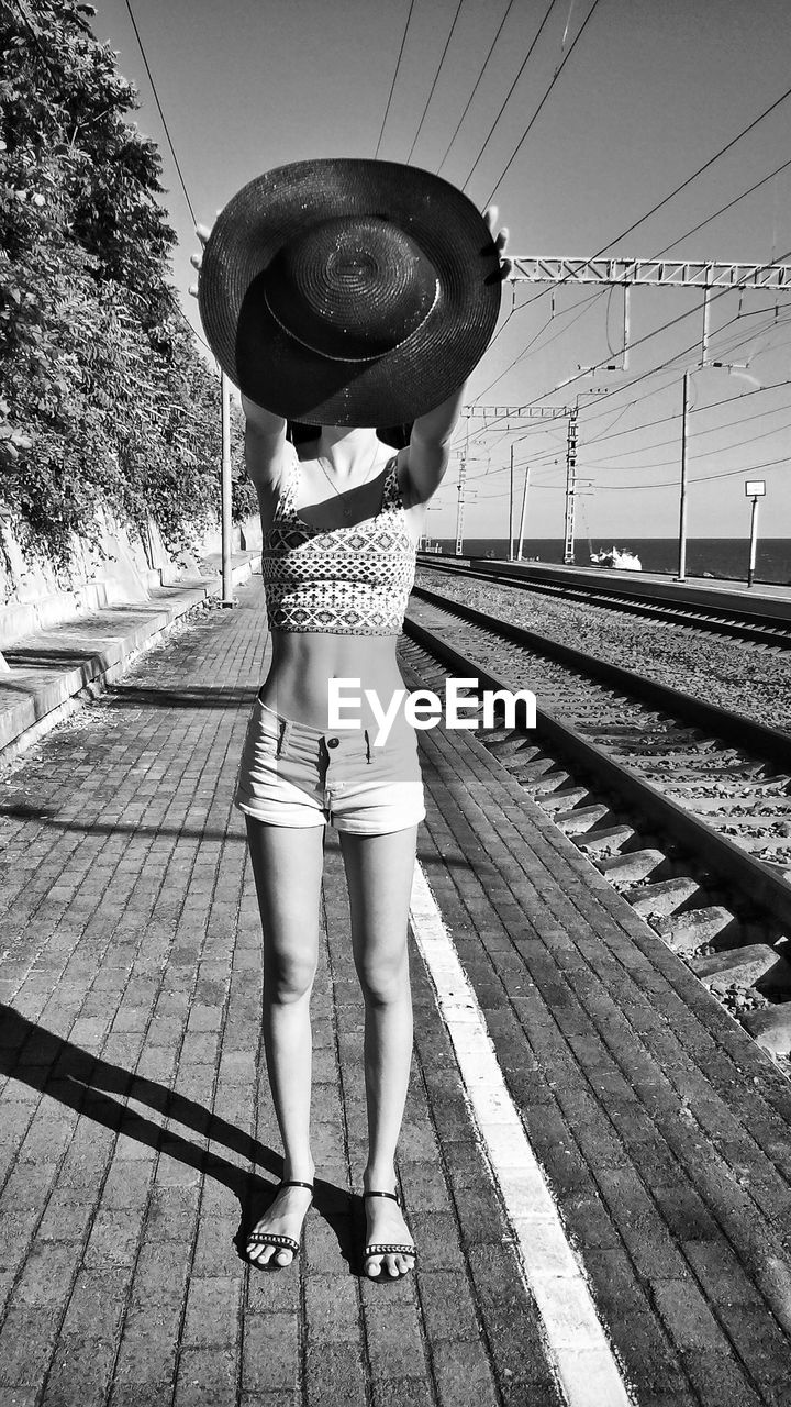 Woman holding hat while standing at railroad station platform