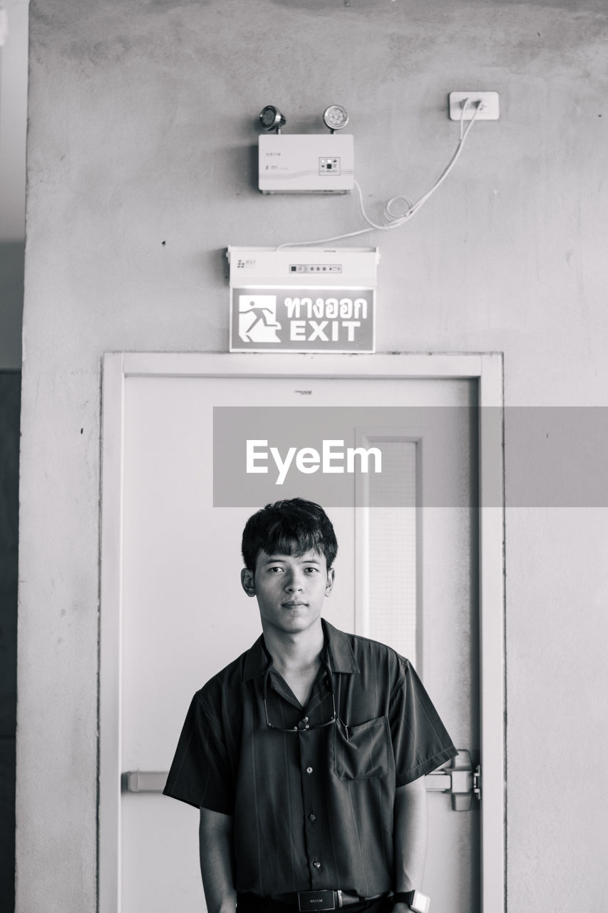 PORTRAIT OF YOUNG MAN STANDING AGAINST DOOR