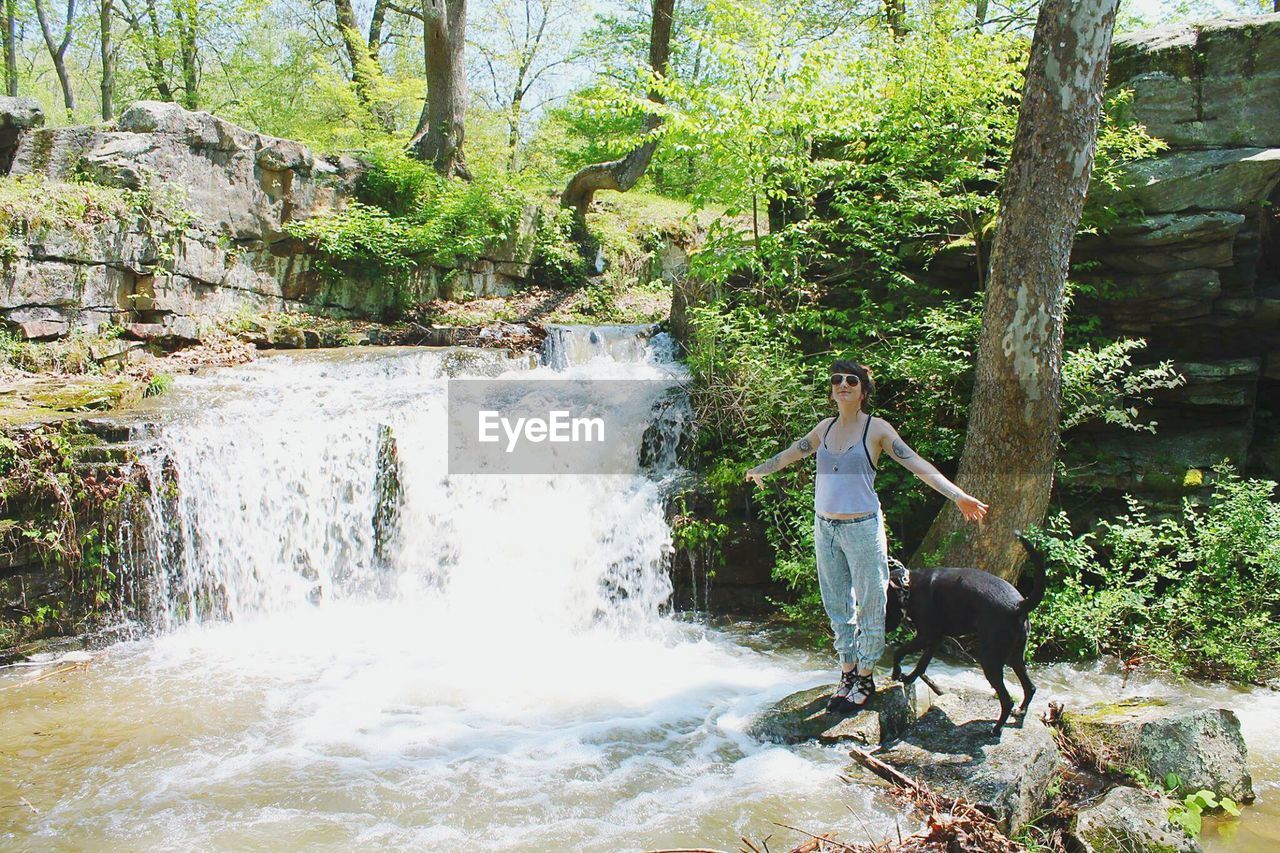 Woman with dog standing near waterfall in forest