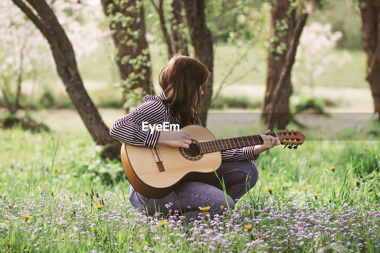 MIDSECTION OF WOMAN PLAYING GUITAR IN FIELD