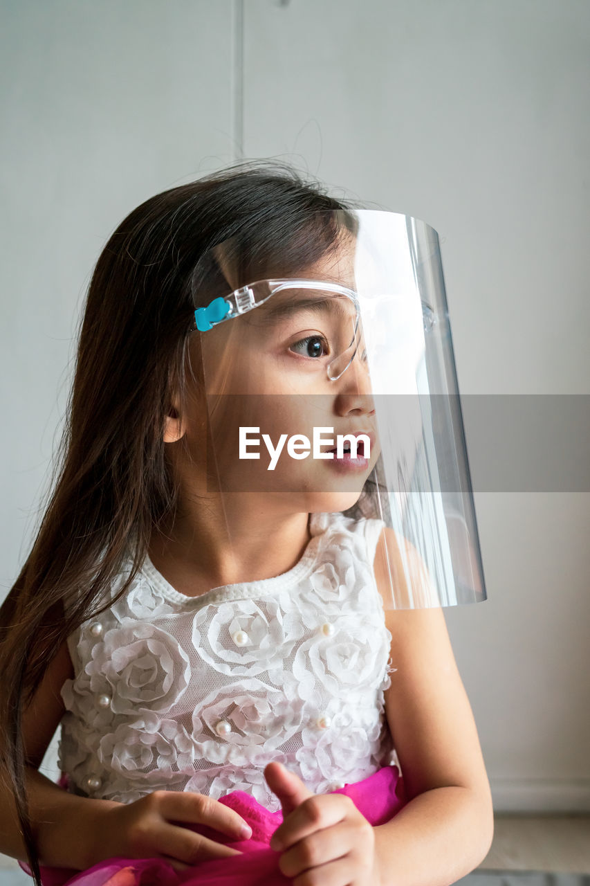 A toddler girl wearing the face protection shield. a safety corona mask during covid-19 pandemic.