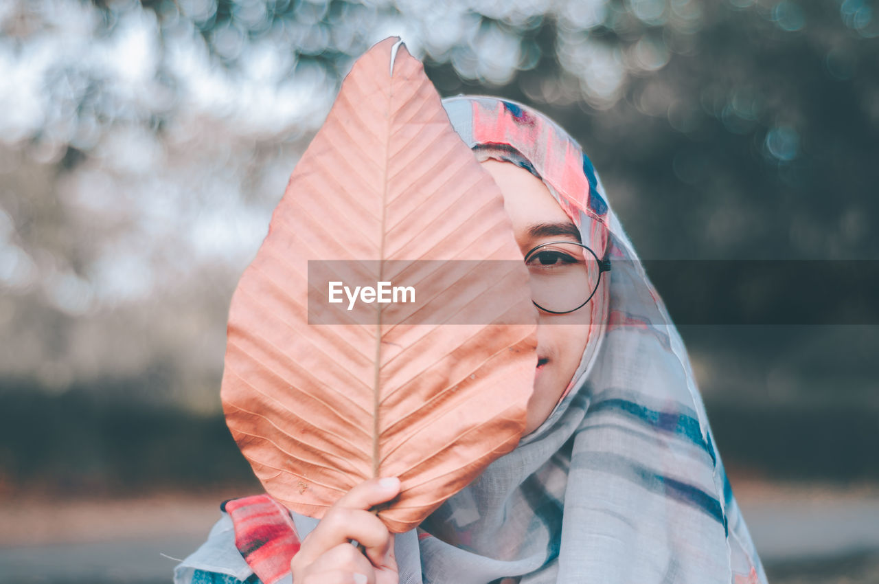 Close-up portrait of teenage girl covering face with dry leaf