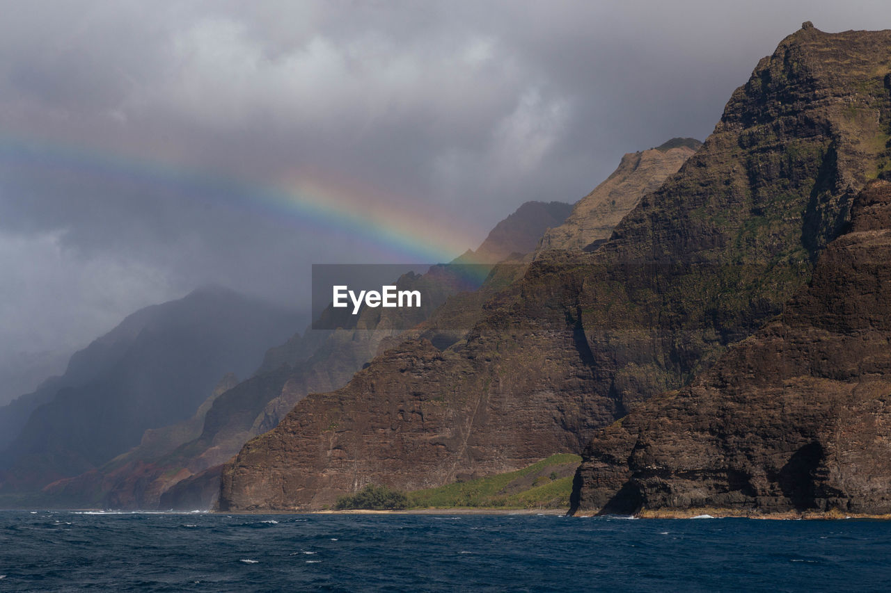 Scenic view of sea and mountains against sky with rainbow, kauai, hawaii