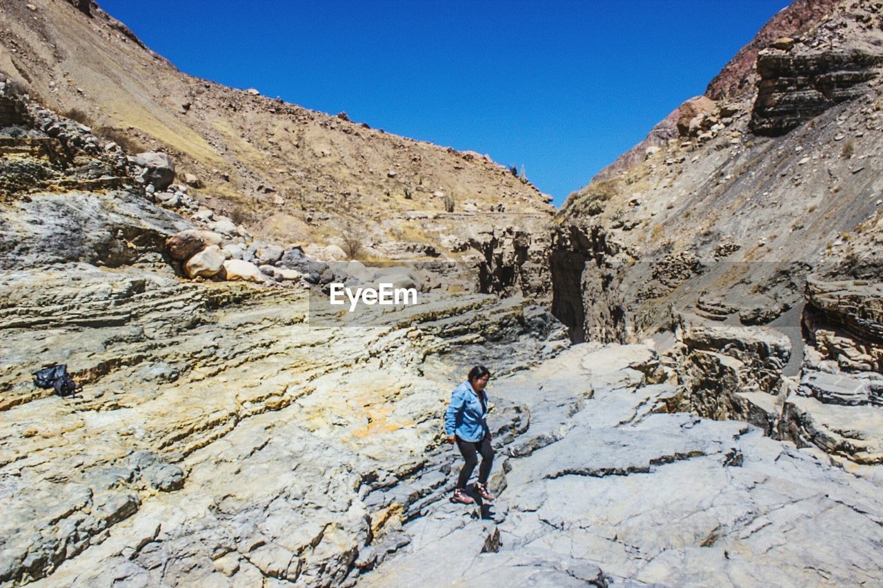 Woman walking on rock formation against clear sky