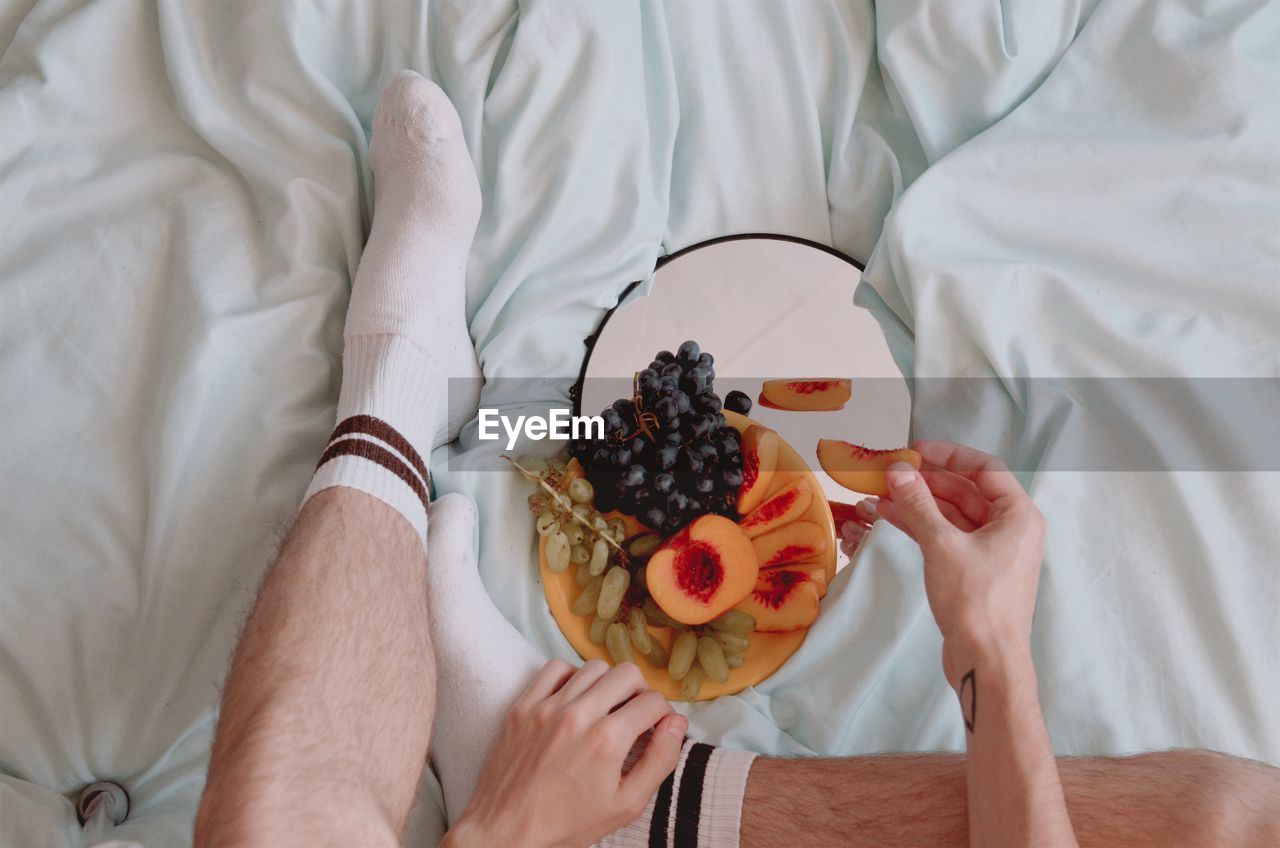 Mens legs on the bed with plate of fruits and mirror