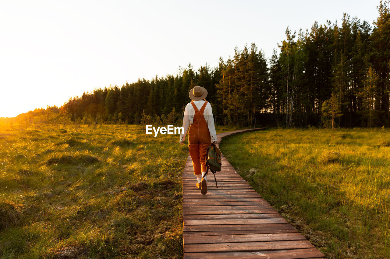 Woman botanist with backpack on ecological hiking trail in summer outdoors.