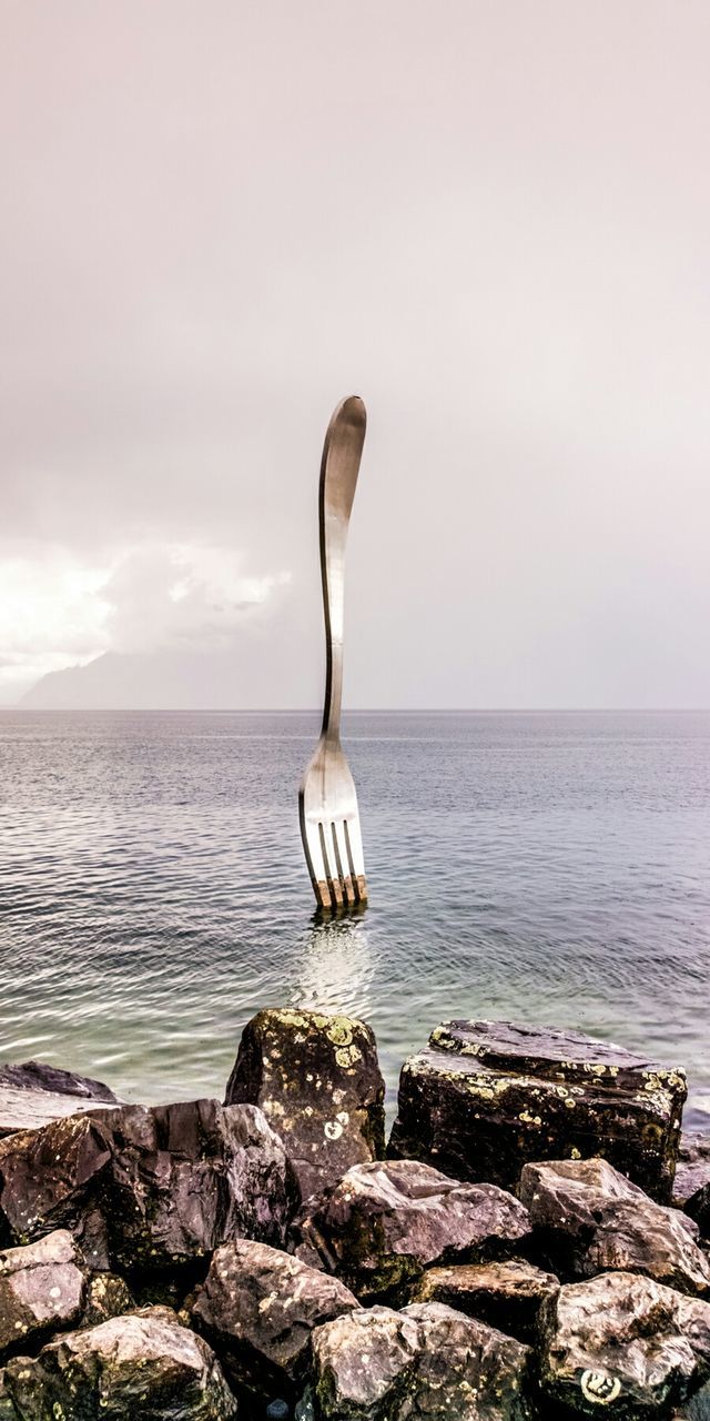 Digital composite image of large fork on sea against sky