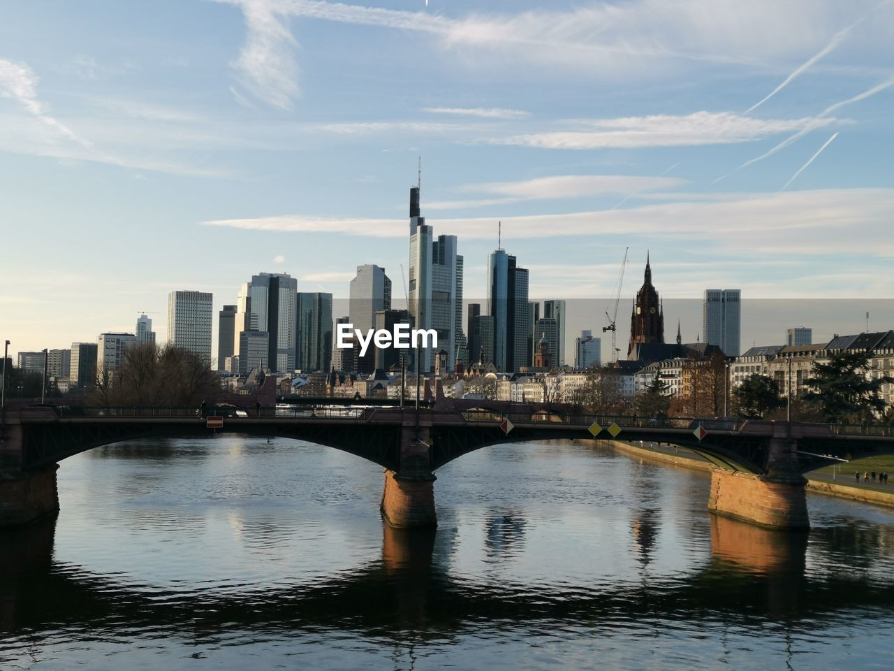 Bridge over river by buildings in city against sky