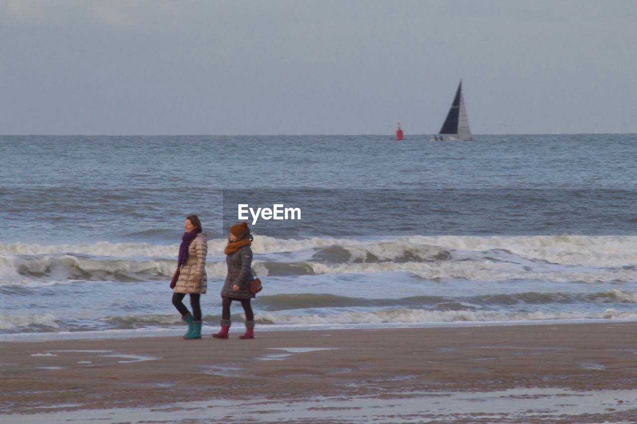 REAR VIEW OF PEOPLE WALKING ON BEACH