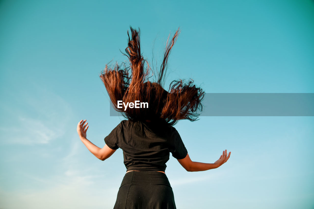 Rear view of woman tossing hair against sky