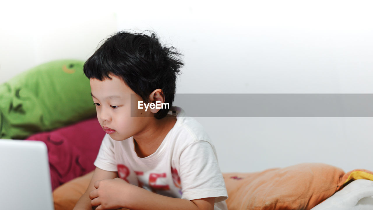 Boy using laptop while sitting on bed at home