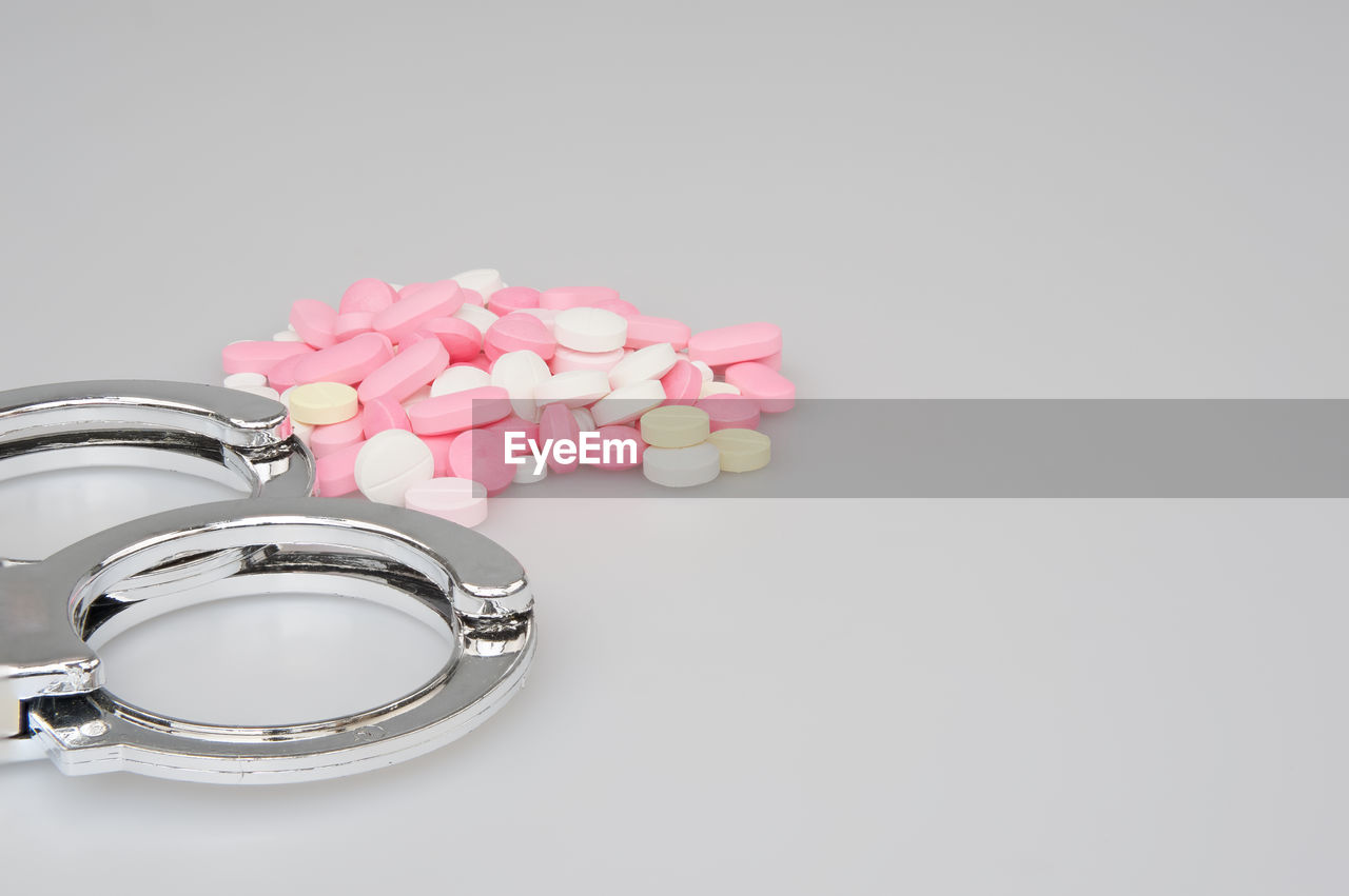 Directly above shot of pills by handcuffs over white background