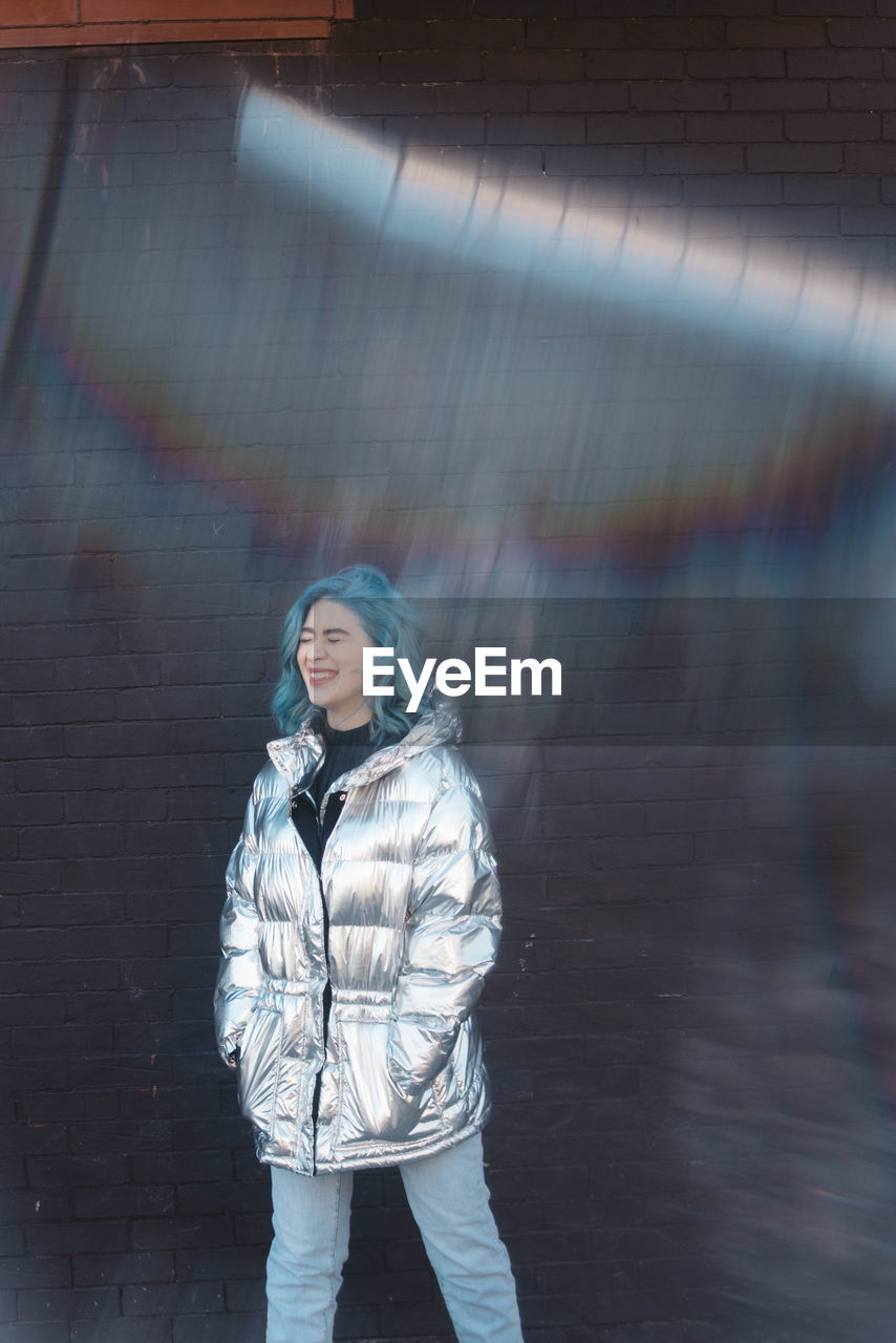 Woman wearing winter jacket while standing against wall