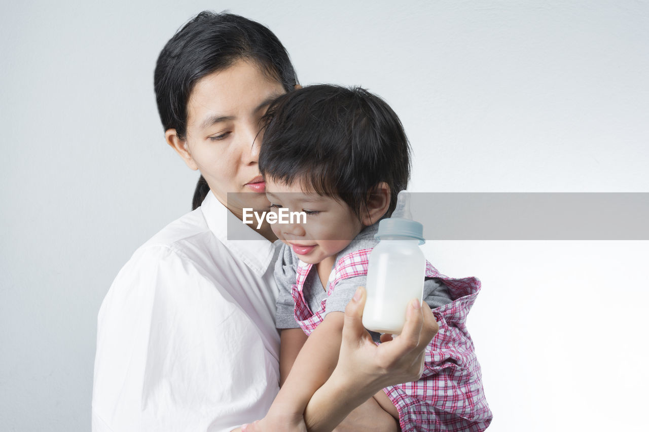 Mother holding milk bottle with daughter against white background
