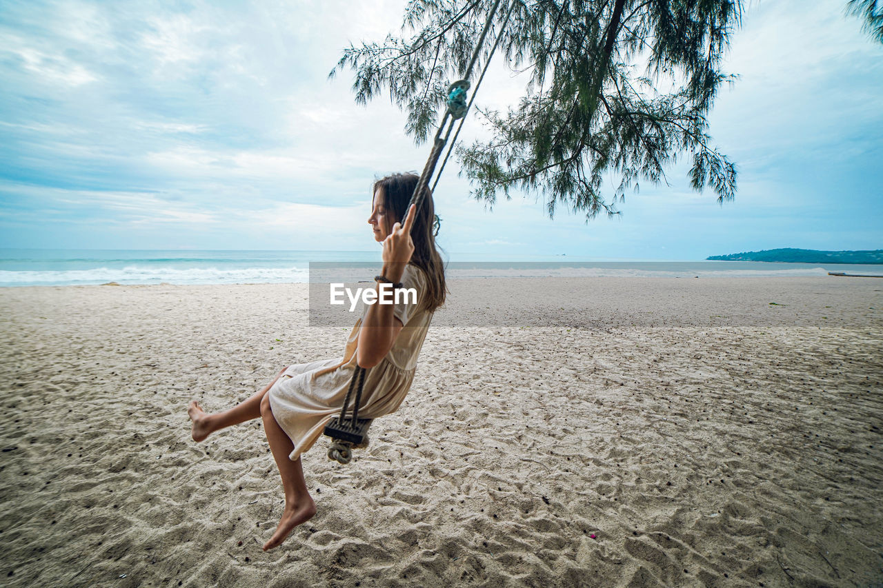 Side view of young woman swinging  on beach