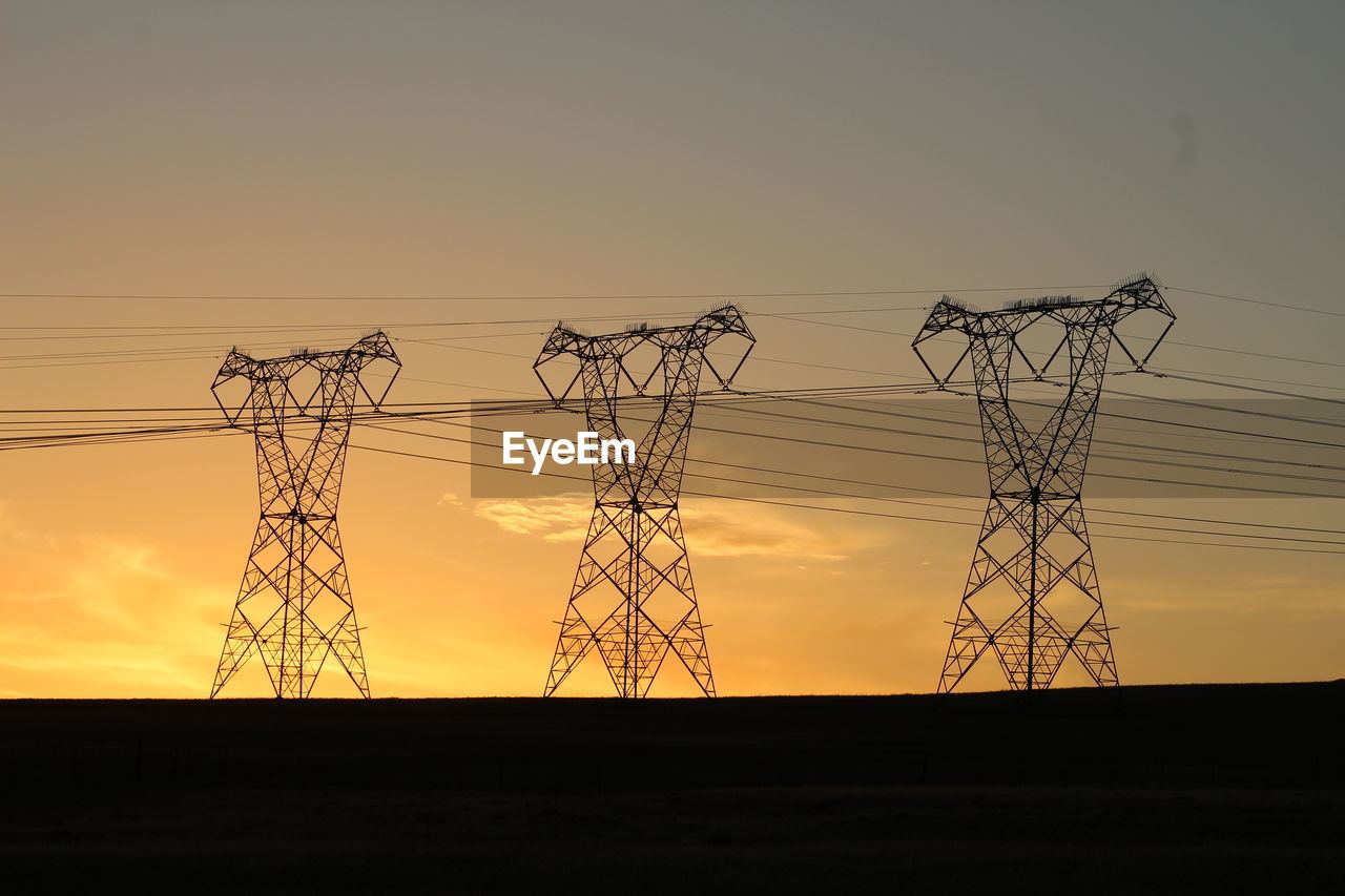 Silhouette electricity pylons on field during sunset