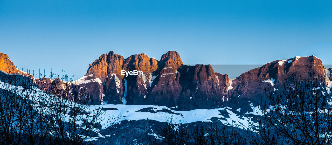 Low angle view of snowcapped mountains against clear blue sky