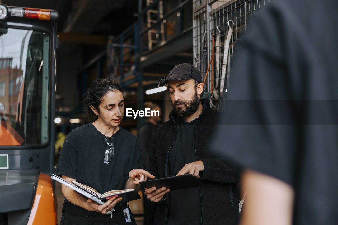 Male employee holding tablet pc while discussing with female colleague in warehouse