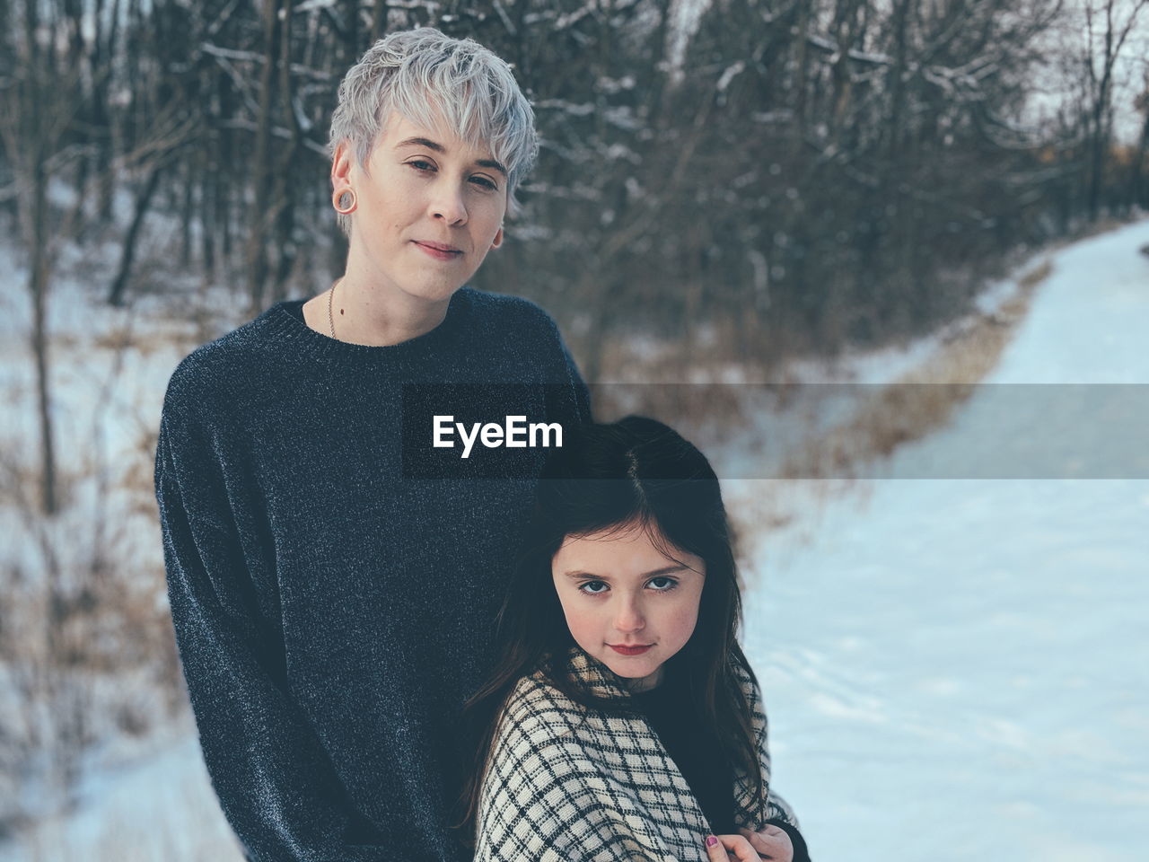 Portrait of smiling young woman with daughter standing on snow covered field