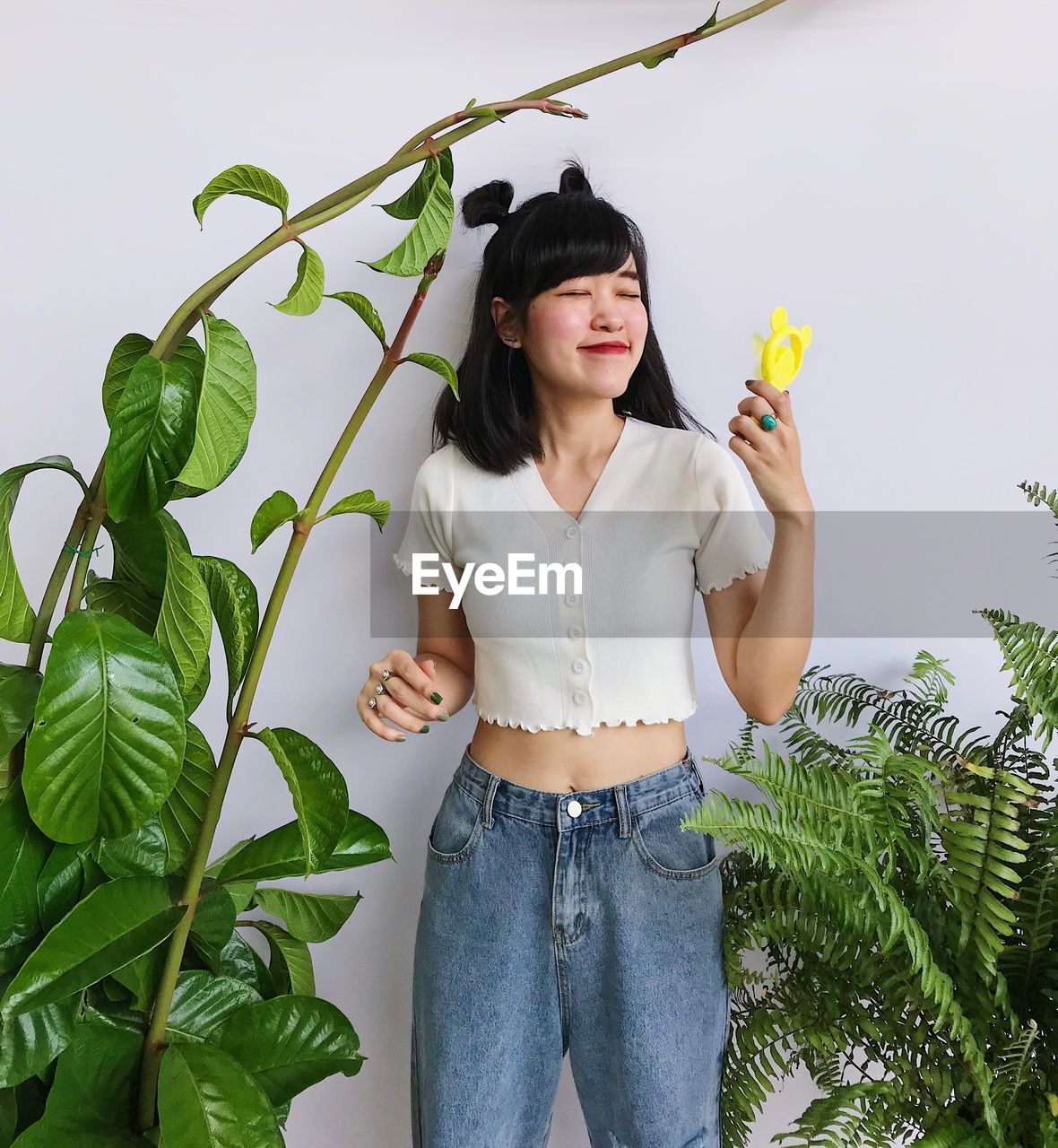 Portrait of asian girl in white crop top and jeans holding a yellow small fan