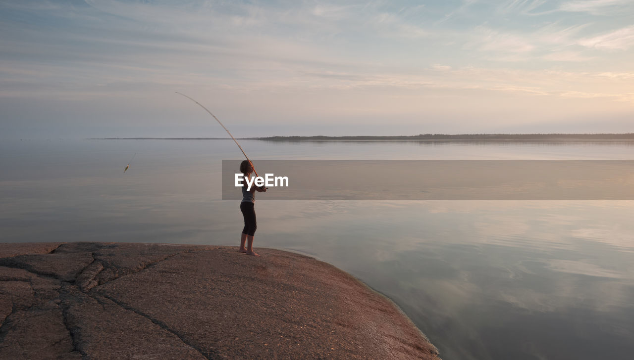 The fisherwoman throws a bait. girl with a fishing rod on a granite shore in a picturesque place.