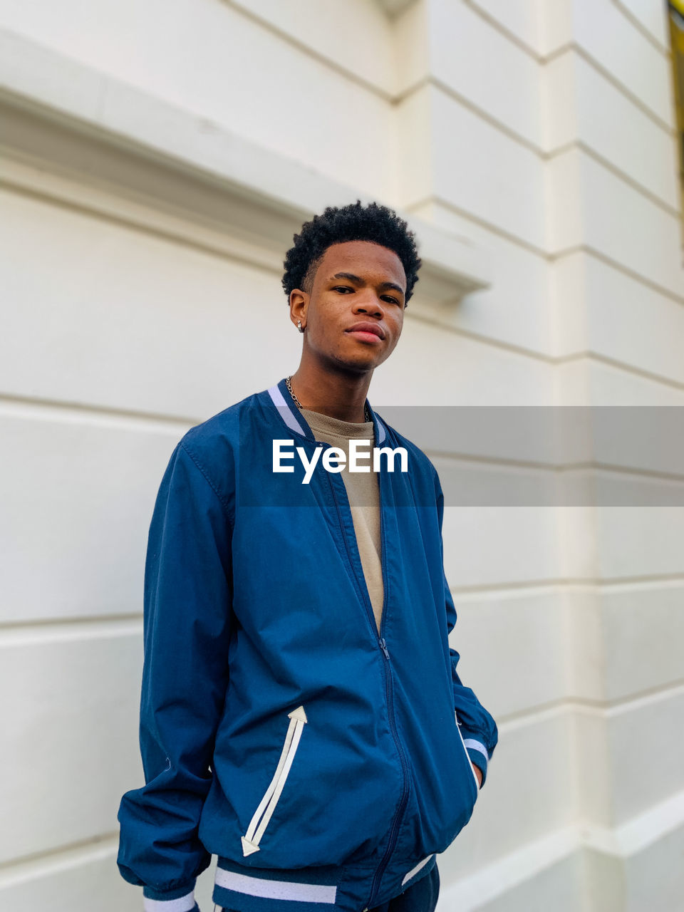 Young male standing against white wall.