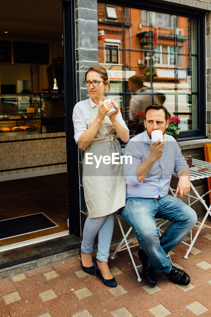 Man and woman, couple of cafe owners drinking tea at entrance of cafe