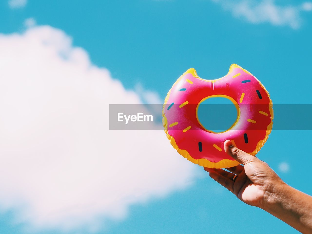 Cropped hand of person holding inflatable donut against sky