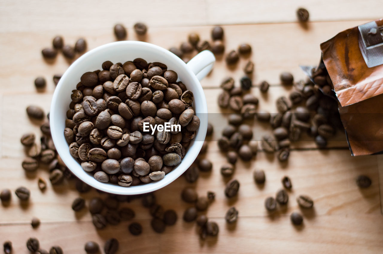 Directly above view of roasted coffee beans scattered by cup on table