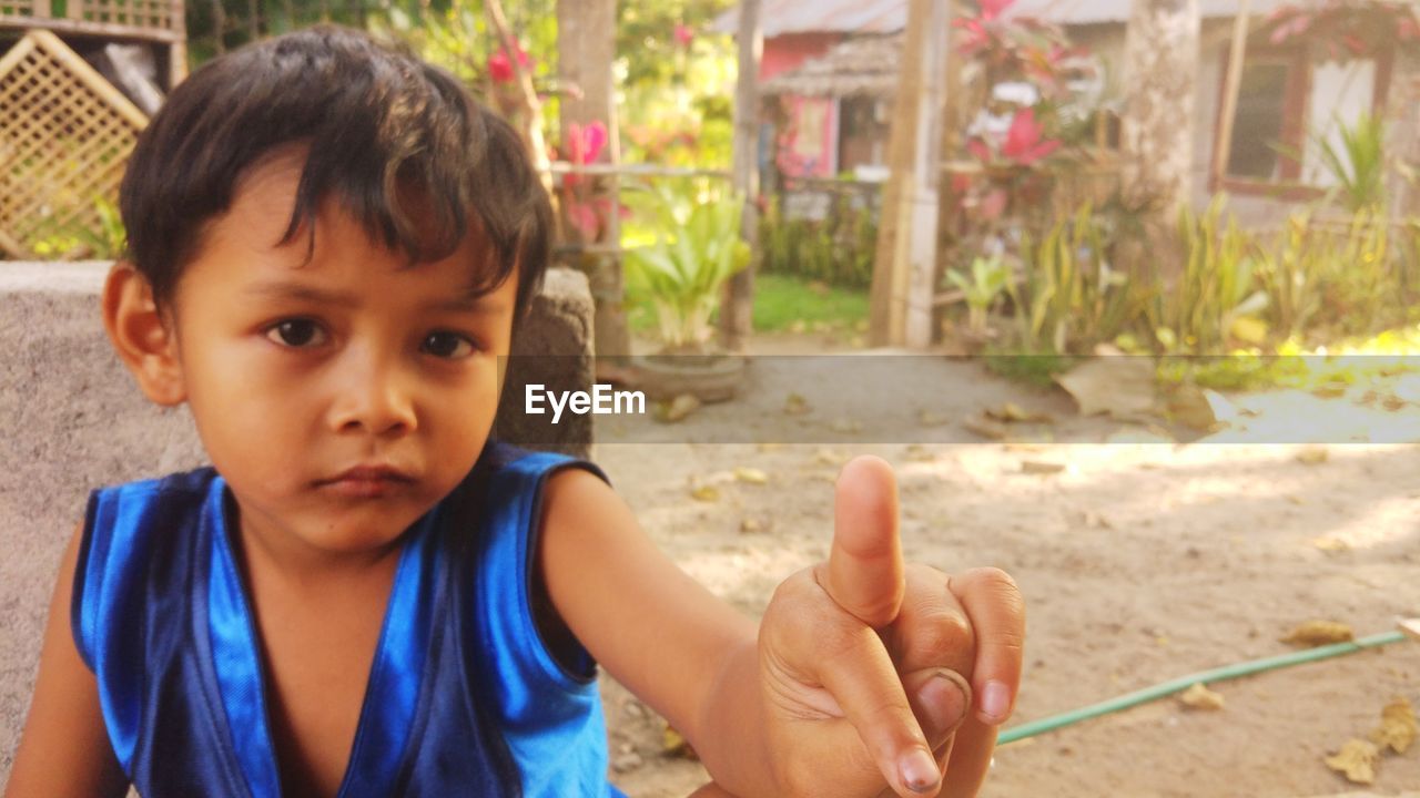 Portrait of boy showing obscene gesture against plants