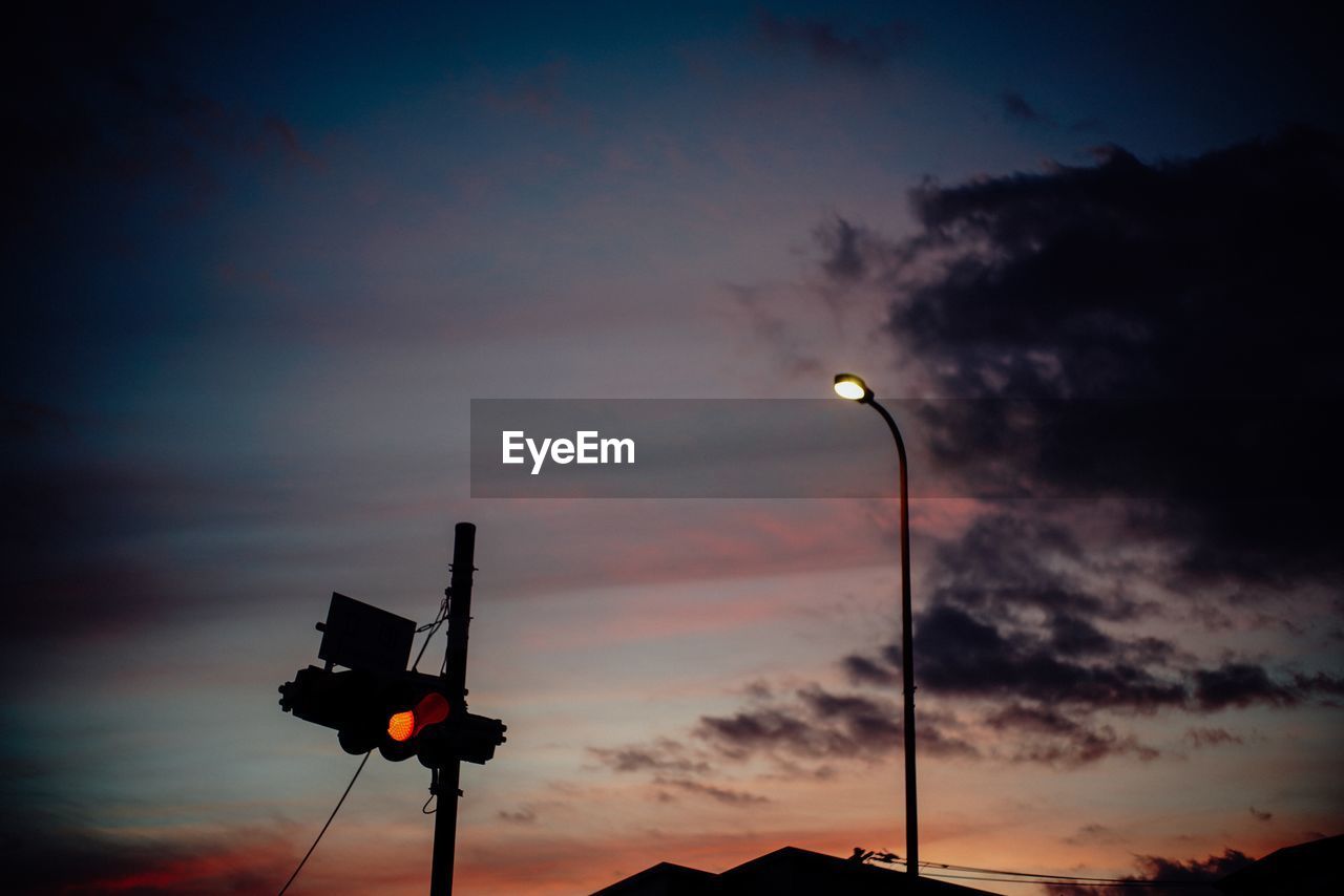 Low angle view of illuminated street light and road signal against sky during sunset