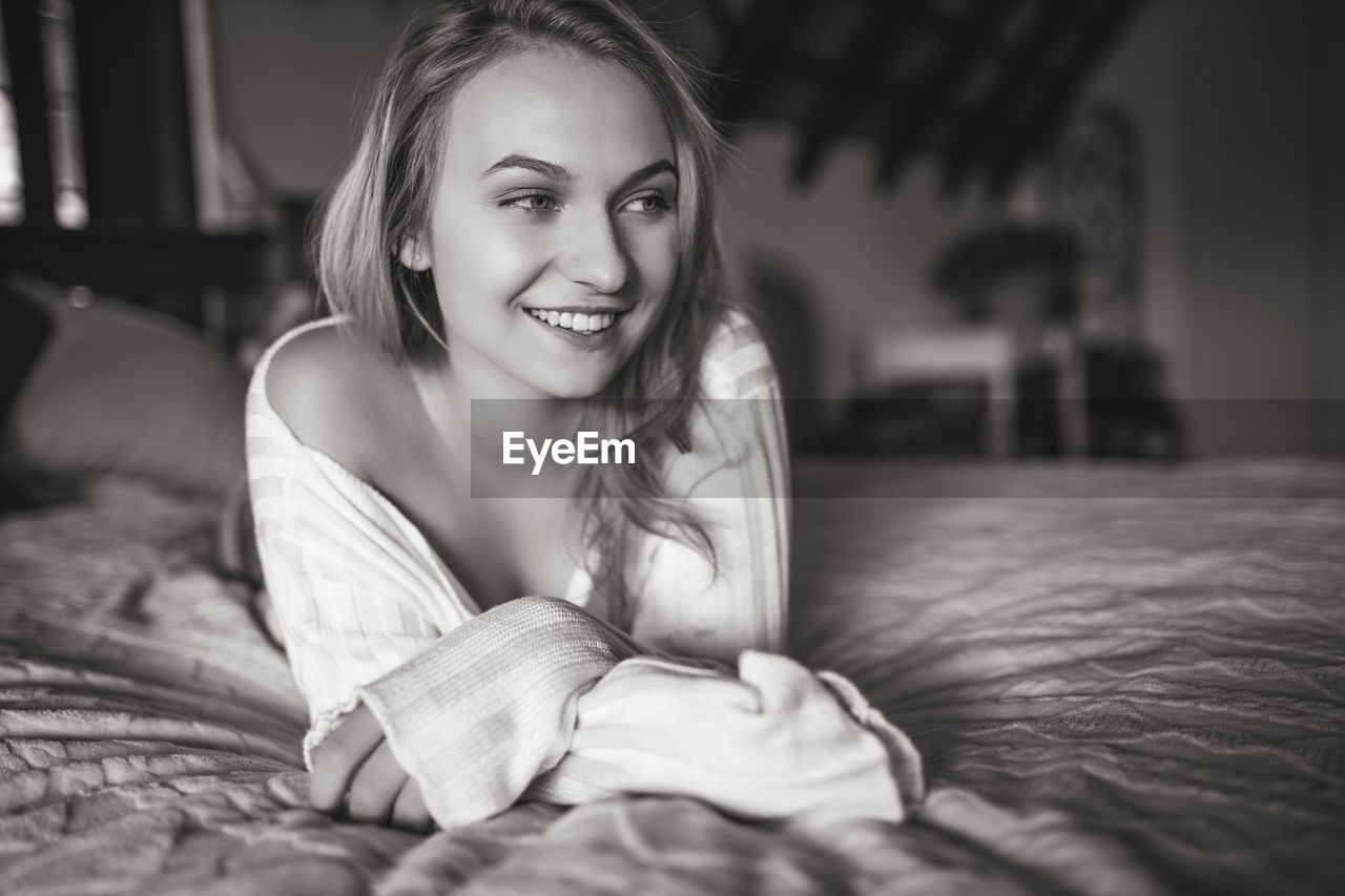 PORTRAIT OF HAPPY WOMAN LYING ON BED