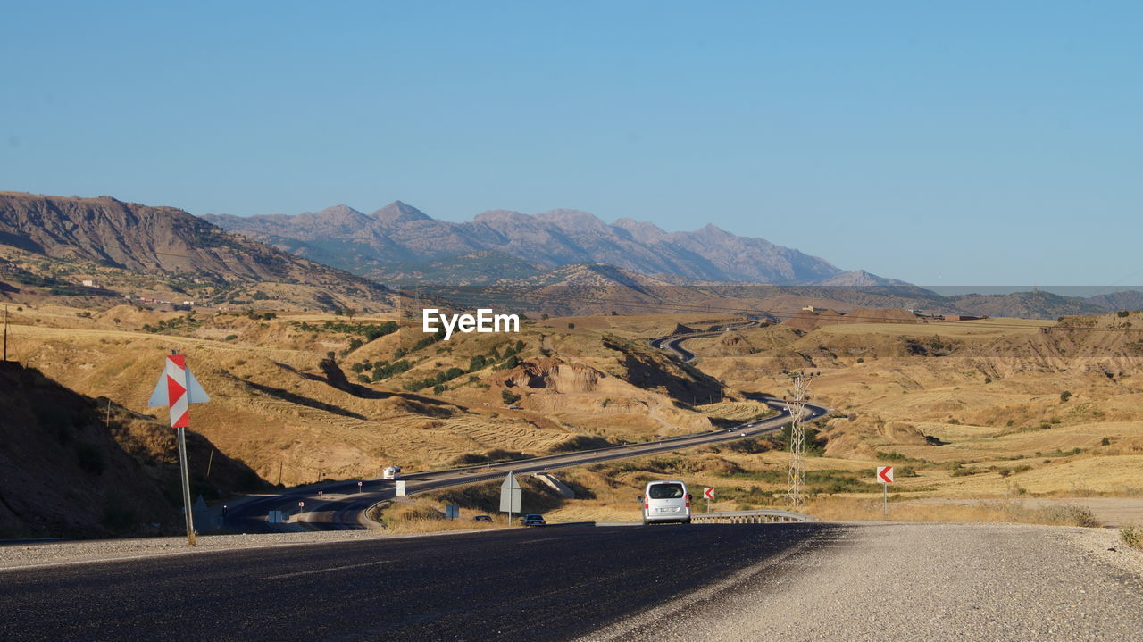 Road leading towards mountains against clear sky