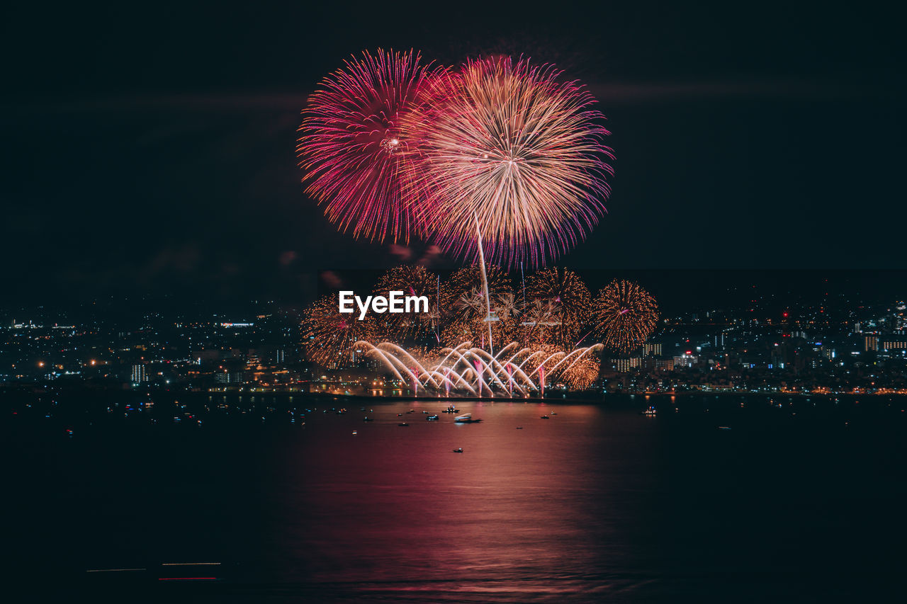 Firework display over illuminated city against clear sky at night