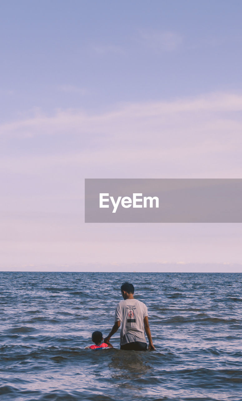 MAN SITTING IN SEA AGAINST SKY