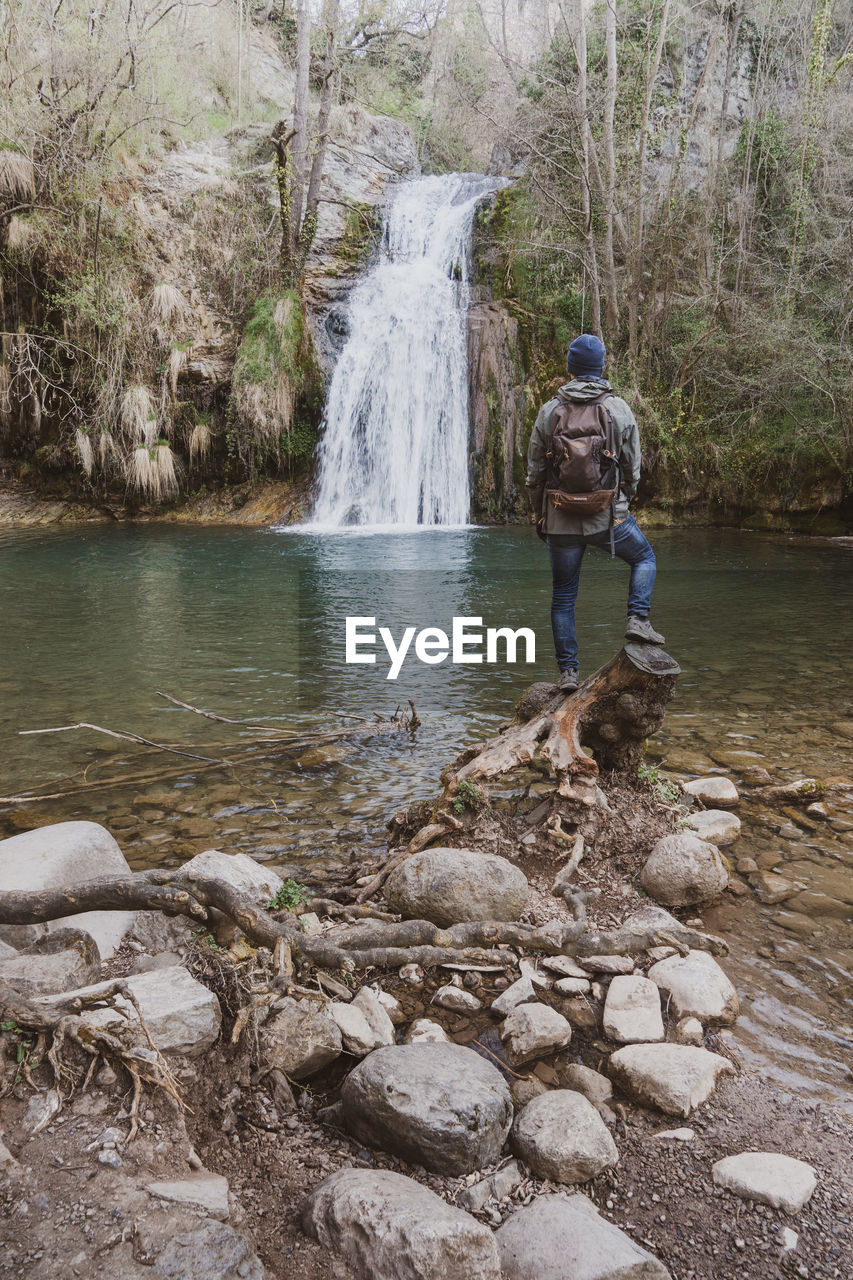 MAN STANDING BY ROCKS IN STREAM