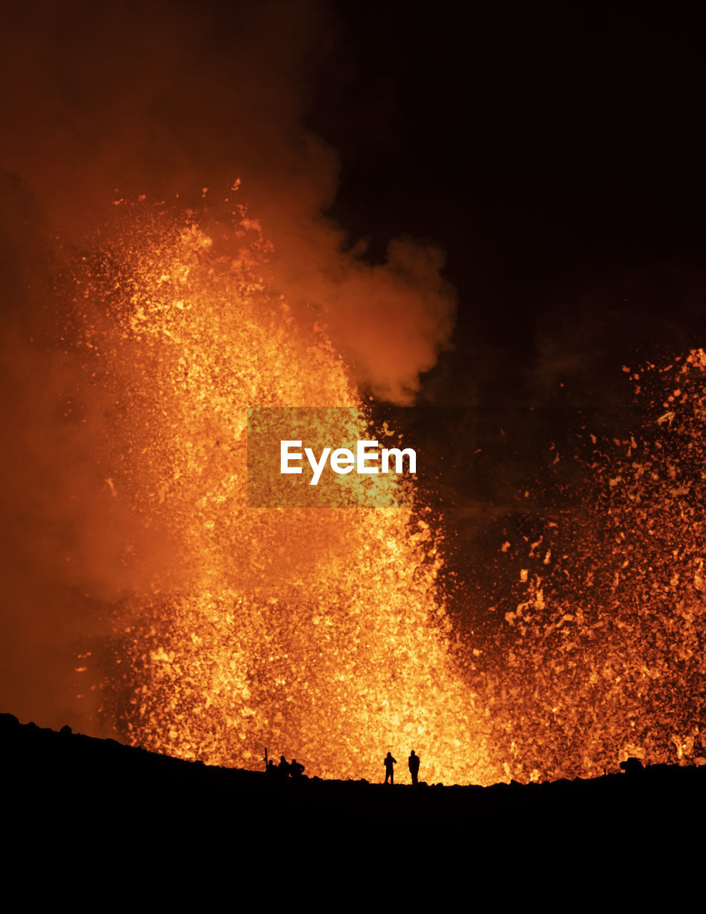 Silhouettes of anonymous travelers standing against orange fume of active volcano in iceland