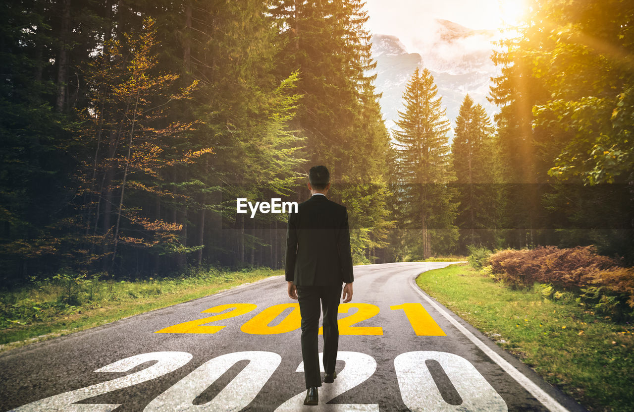 REAR VIEW OF MAN STANDING ON ROAD