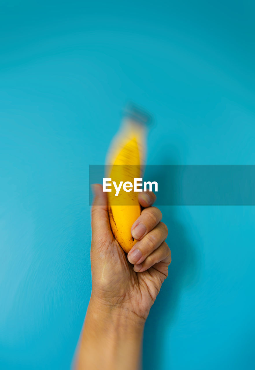 Cropped hand of man holding banana against blue background