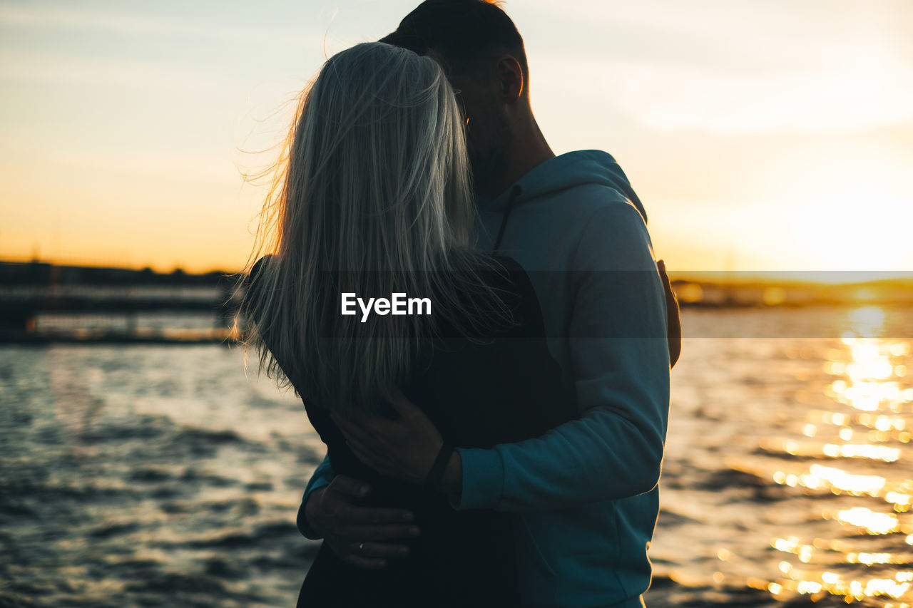 Couple embracing while standing against sea during sunset