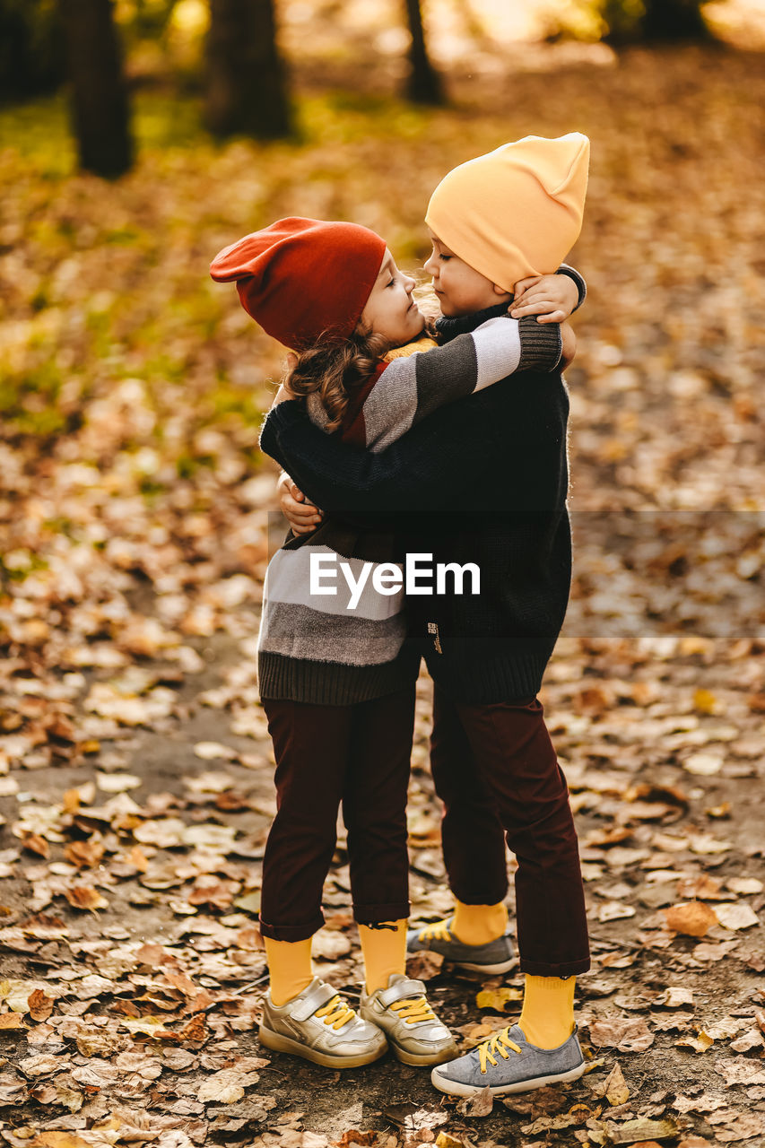 Happy cheerful children in warm clothes have fun walking running in autumn park playing with leaves