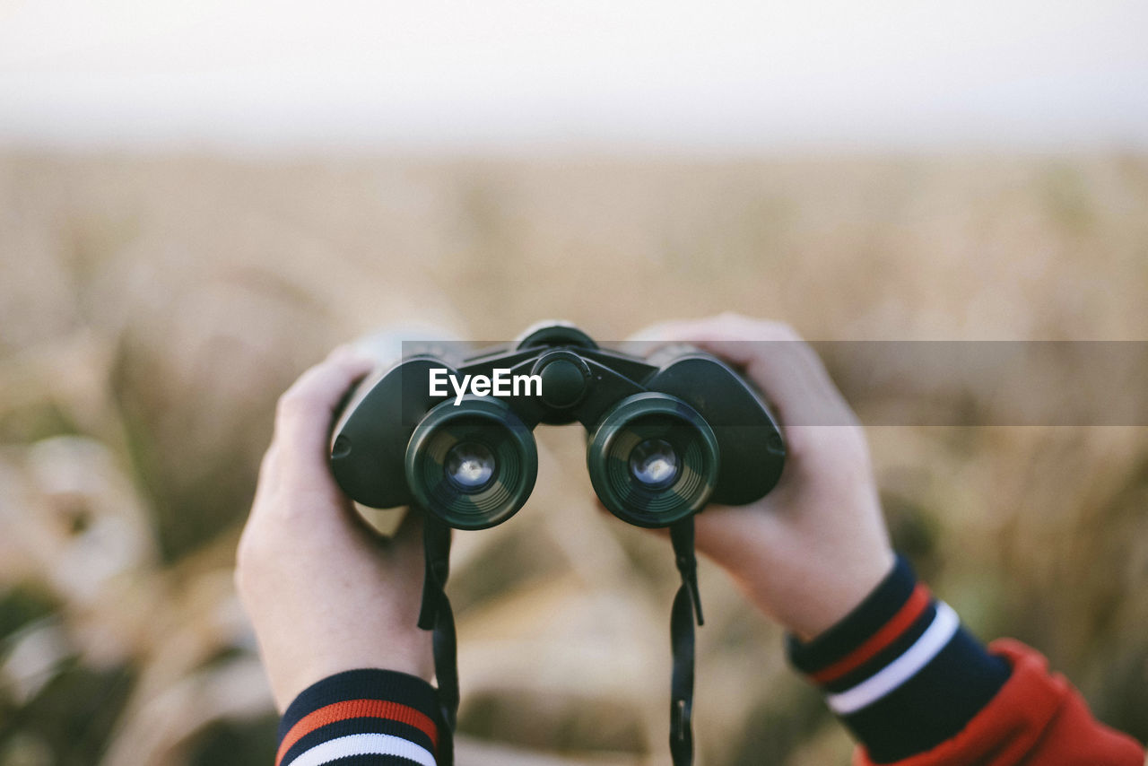 Cropped hands of woman holding binoculars at farm