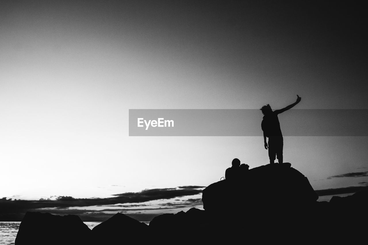 Silhouette man taking selfie on rock against sky at beach