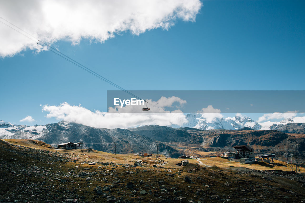 Low angle view of overhead cable car over mountains against sky