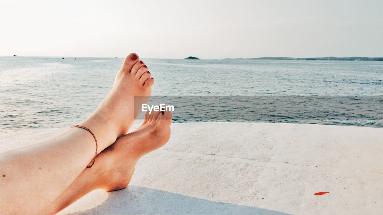 Low section of woman relaxing by sea against sky