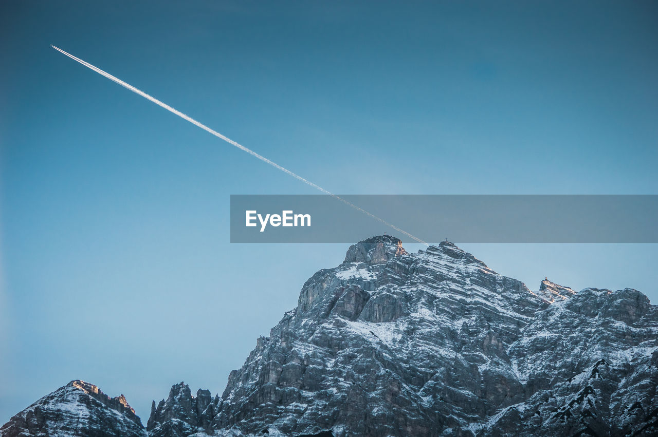 Low angle view of snowcapped mountains against vapor trail in sky