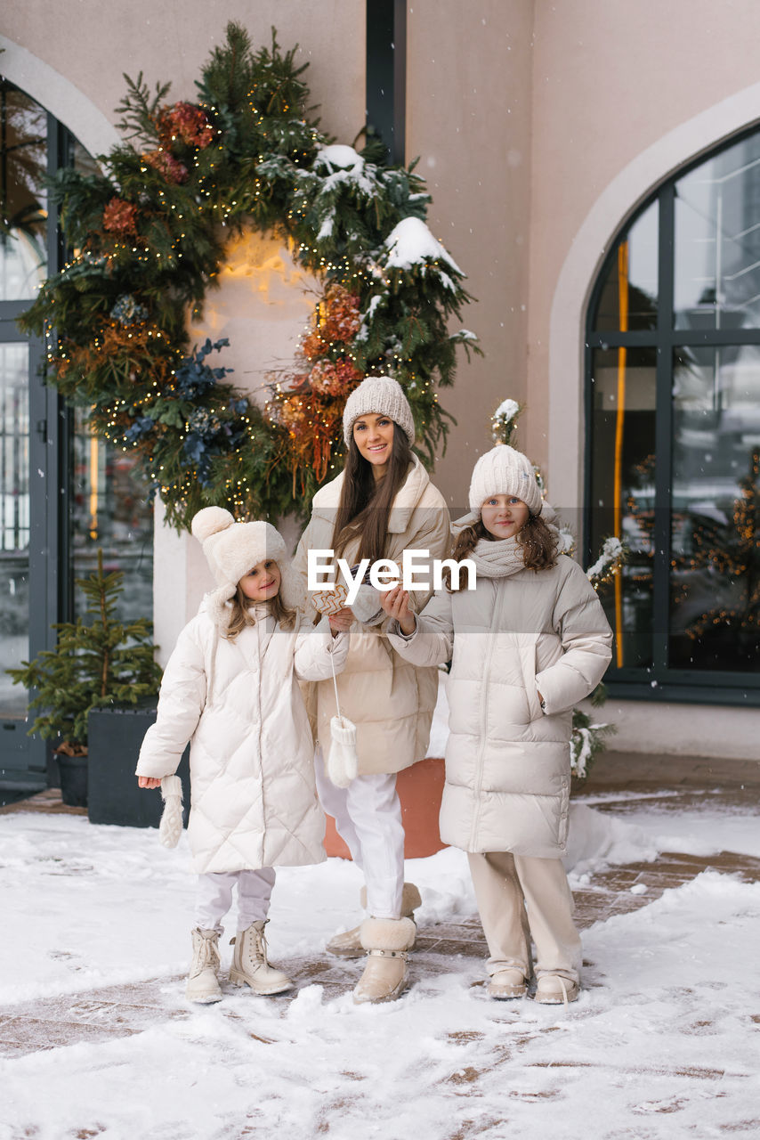Happy young woman mom and two children stand in front of a christmas wreath