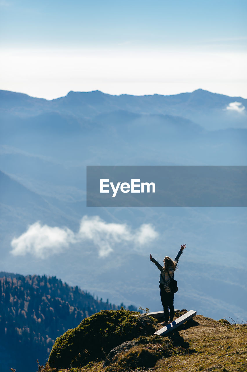 MAN WITH ARMS RAISED AGAINST MOUNTAINS